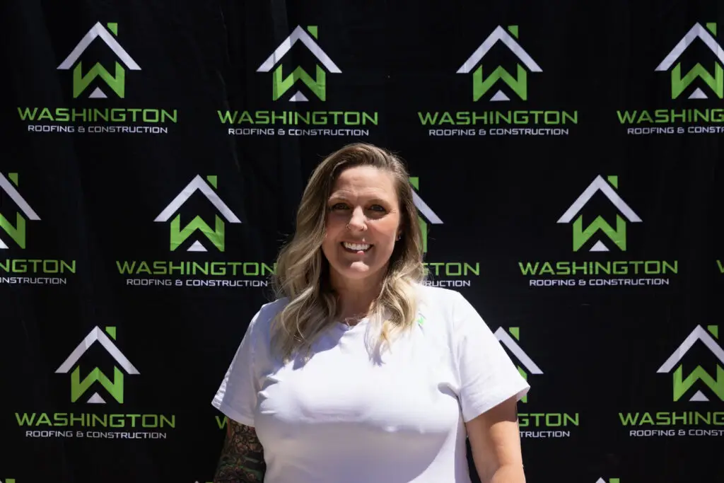 - Washington Roofing & Construction team member Abby Murphy - production manager. standing in front of a backdrop featuring the logo and name "Washington Roofing & Construction.