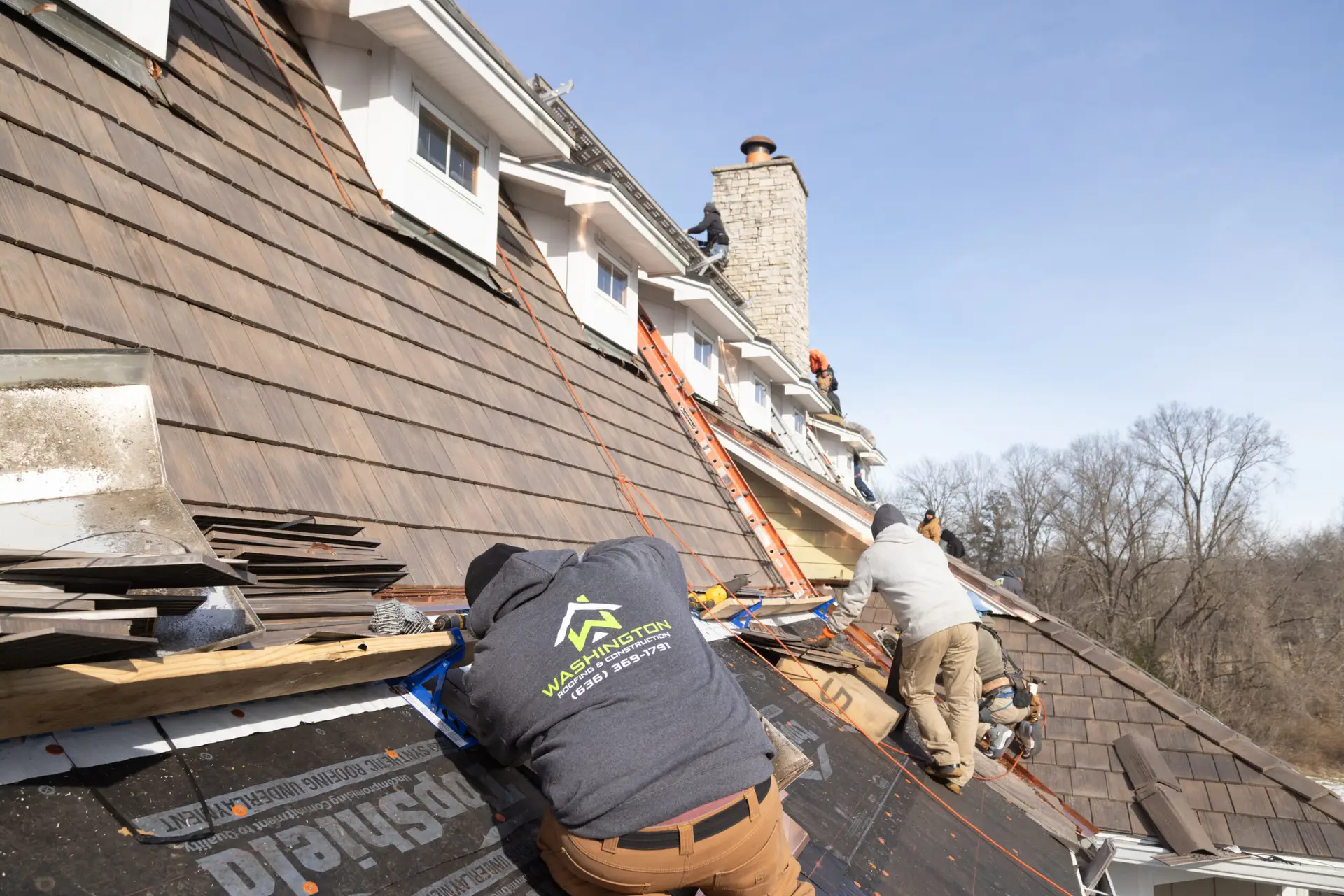 A crew member of Washington Roofing performing roofing services on a large residential home